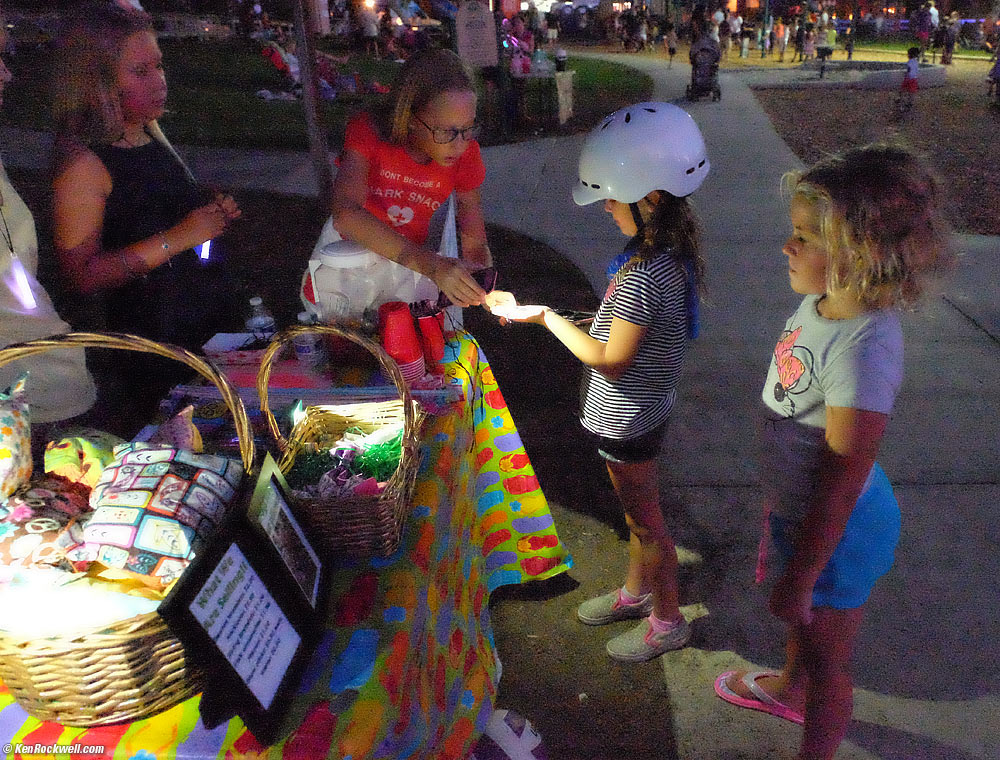 Katie looks at the table selling kid-made pillows and necklaces in the park