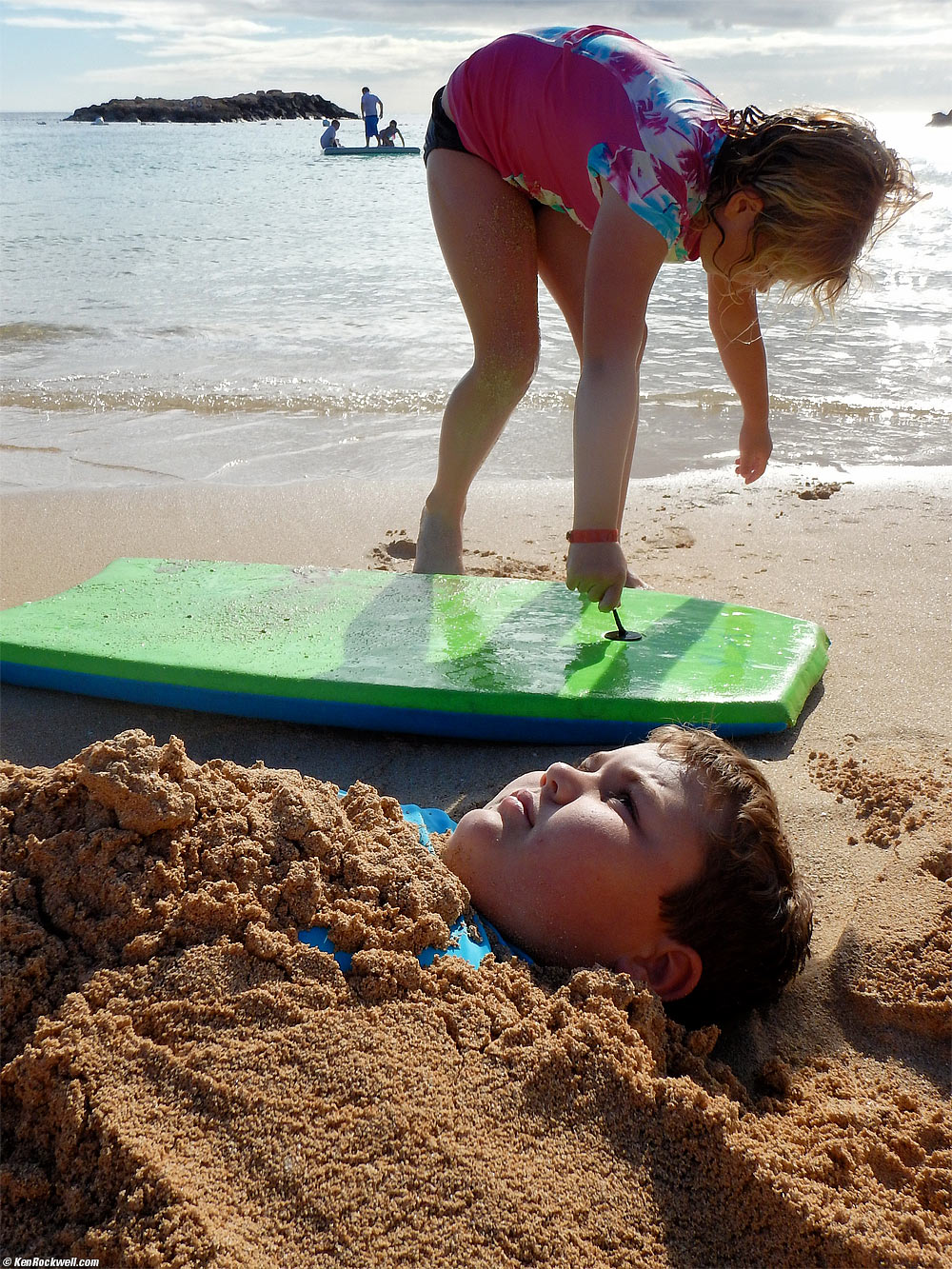 Ryan buried in the sand with Katie above him
